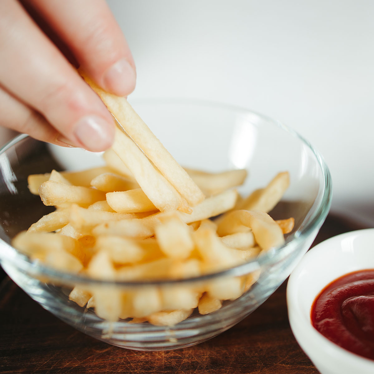 small glass bowl of french fries beside small bowl of ketchup