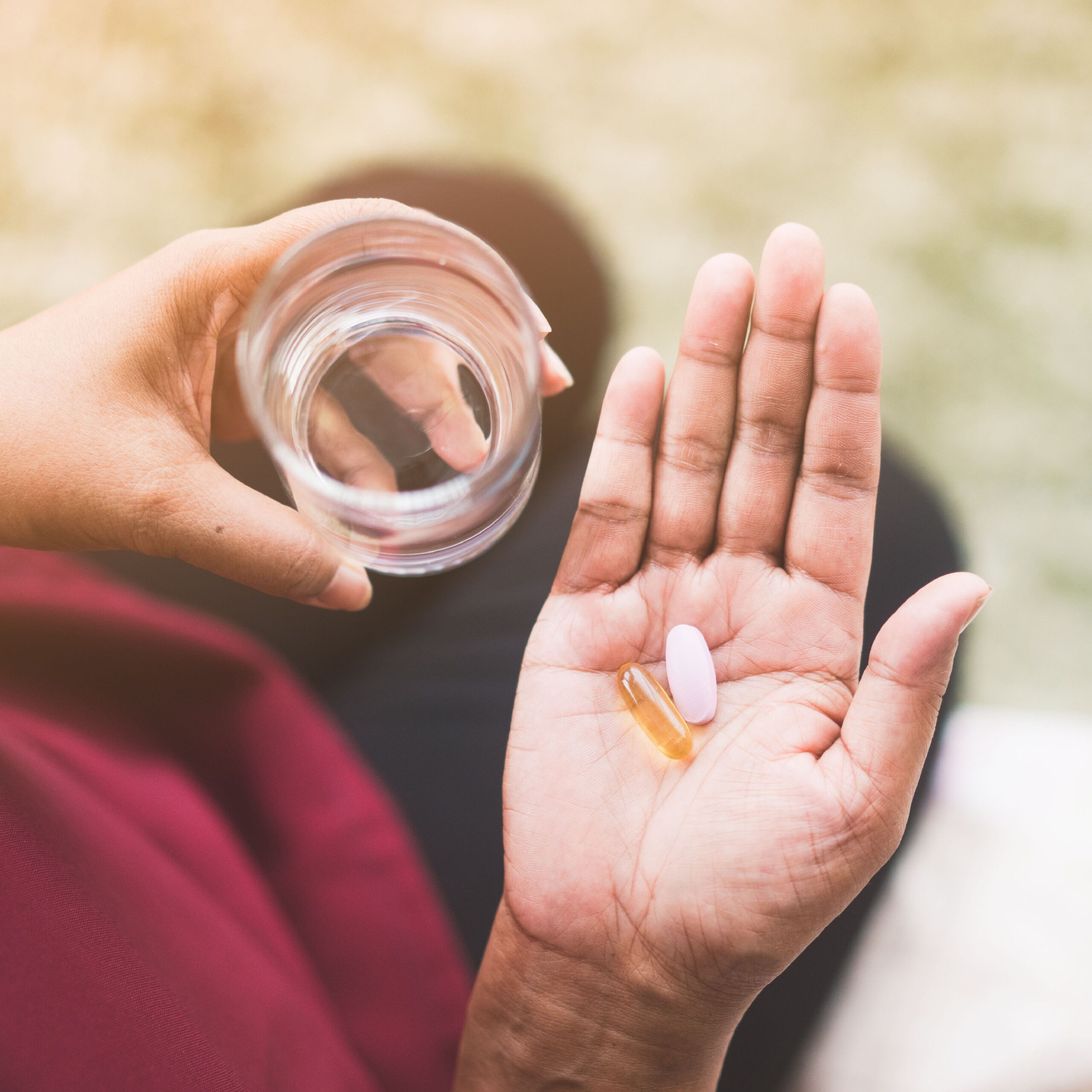 person holding two supplements and a glass of water