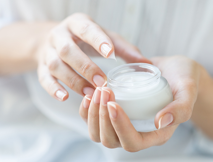 dipping finger into clear jar of moisturizing white cosmetic skincare cream