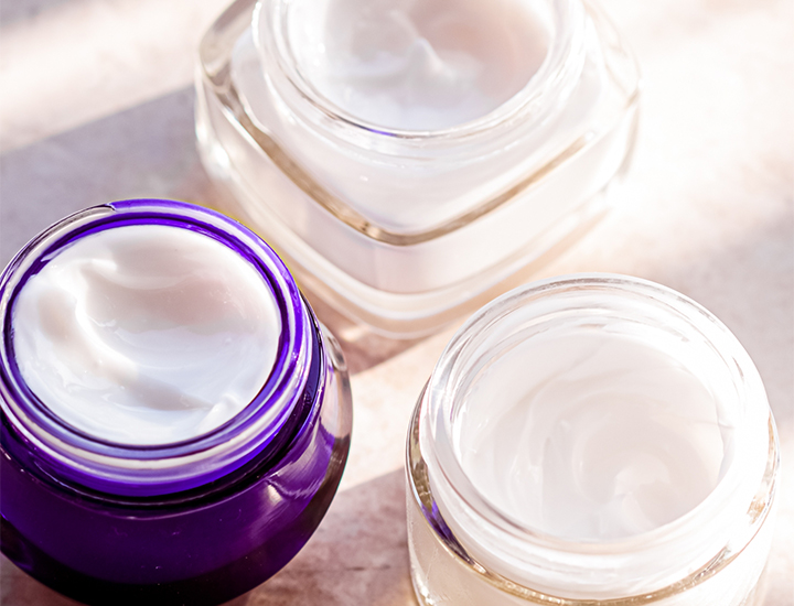 jars of cosmetic white cream sunscreen moisturizer product purple clear containers opened isolated