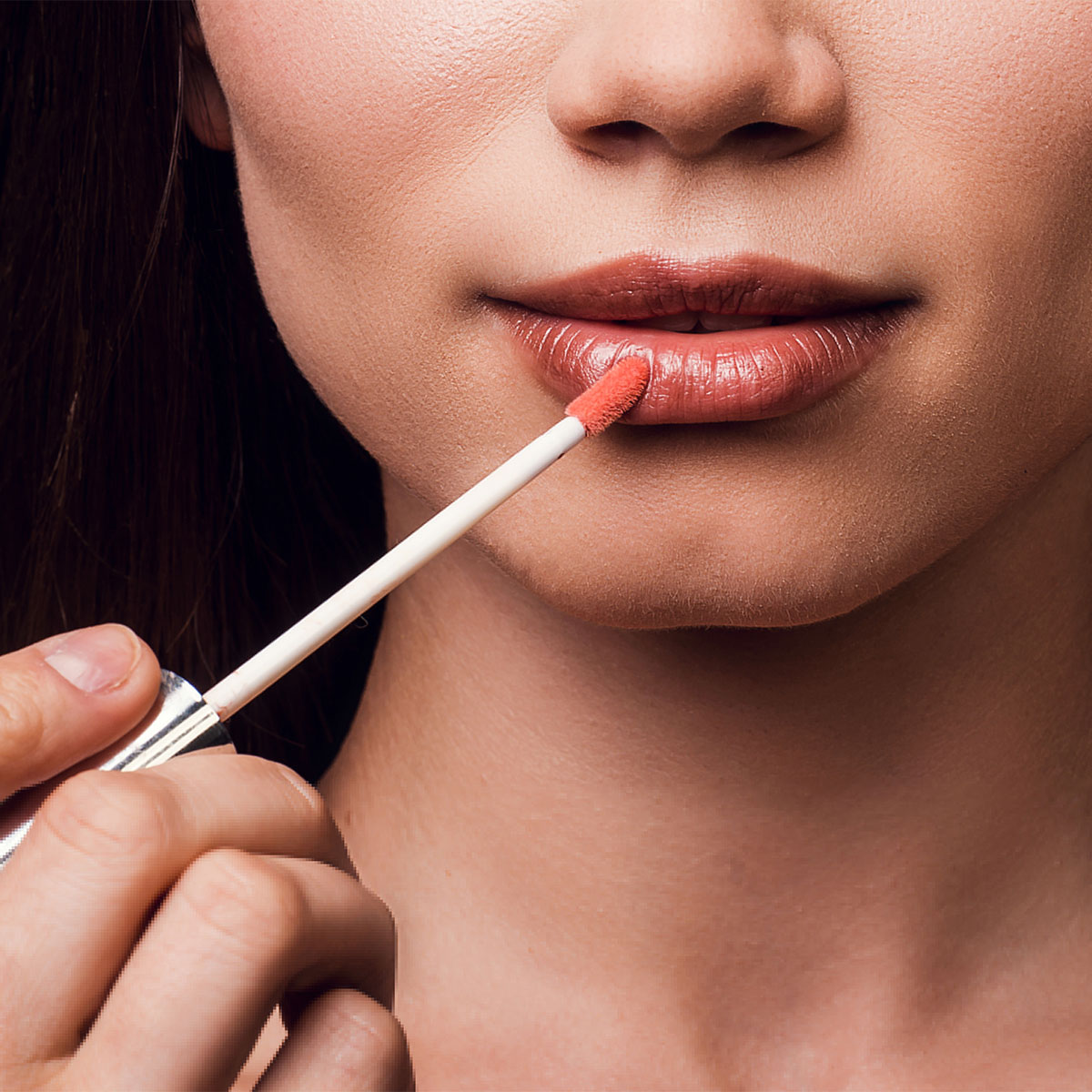 woman applying pink lip gloss to full lips white wand