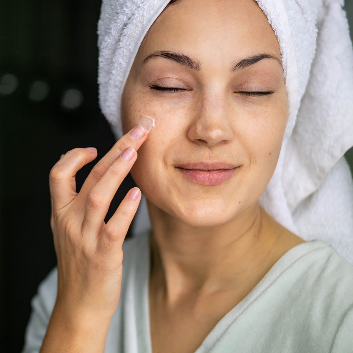 woman applying sunscreen to face white towel turban eyes closed