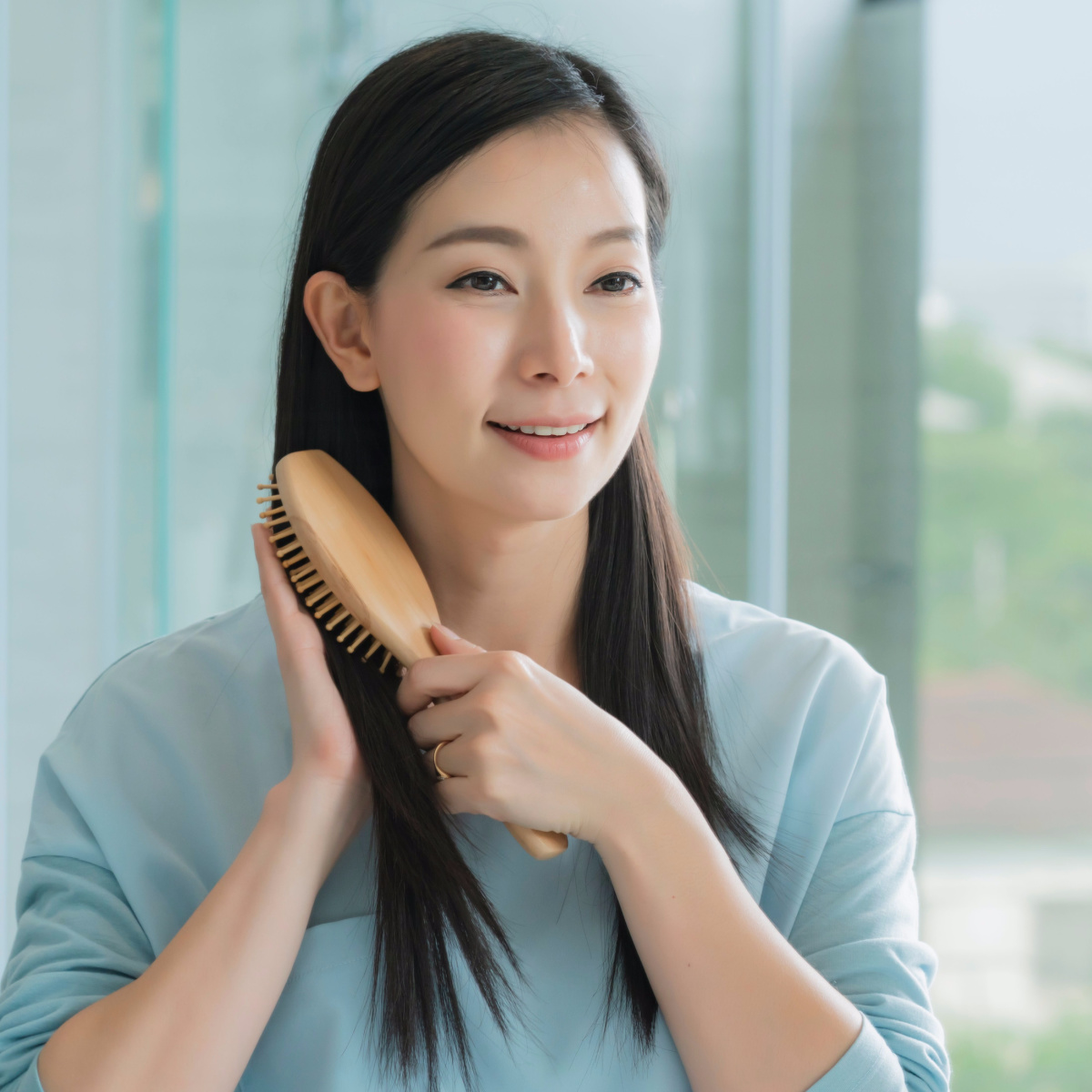 woman brushing long straight dark hair side part blue shirt