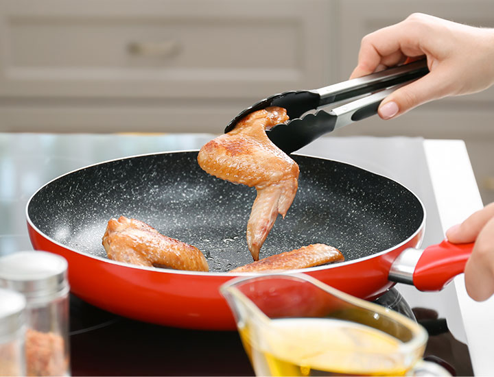 Woman cooking chicken wings in a pan
