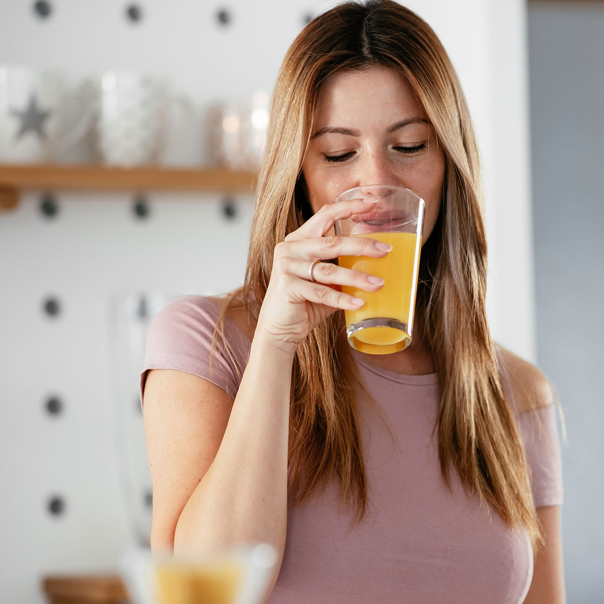 woman drinking glass of orange juice in kitchen