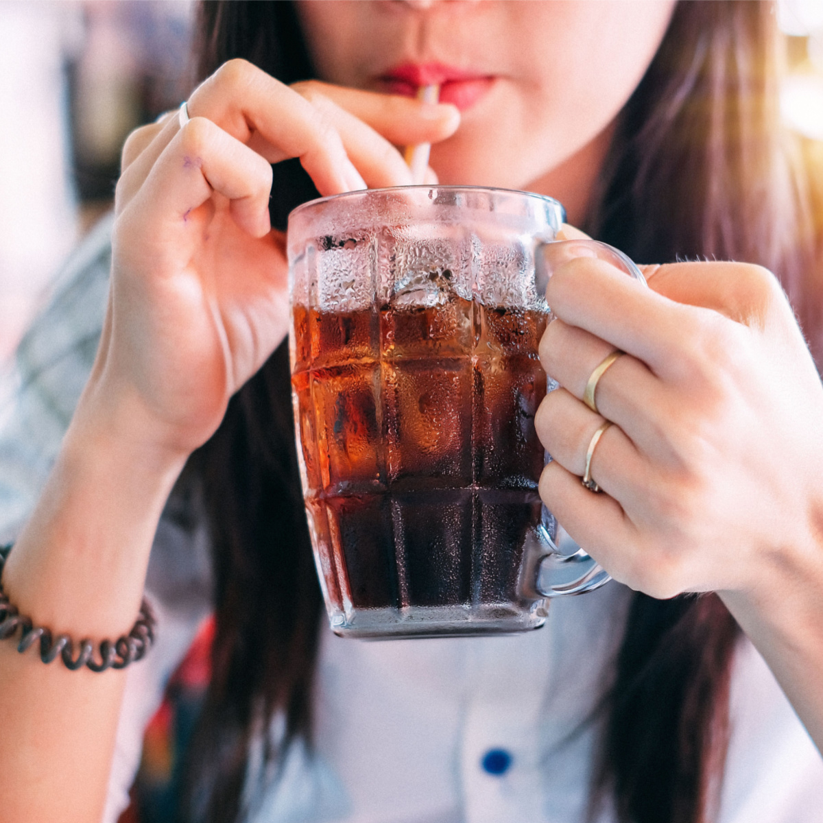 woman drinking brown soda carbonated drink through straw in drinking glass