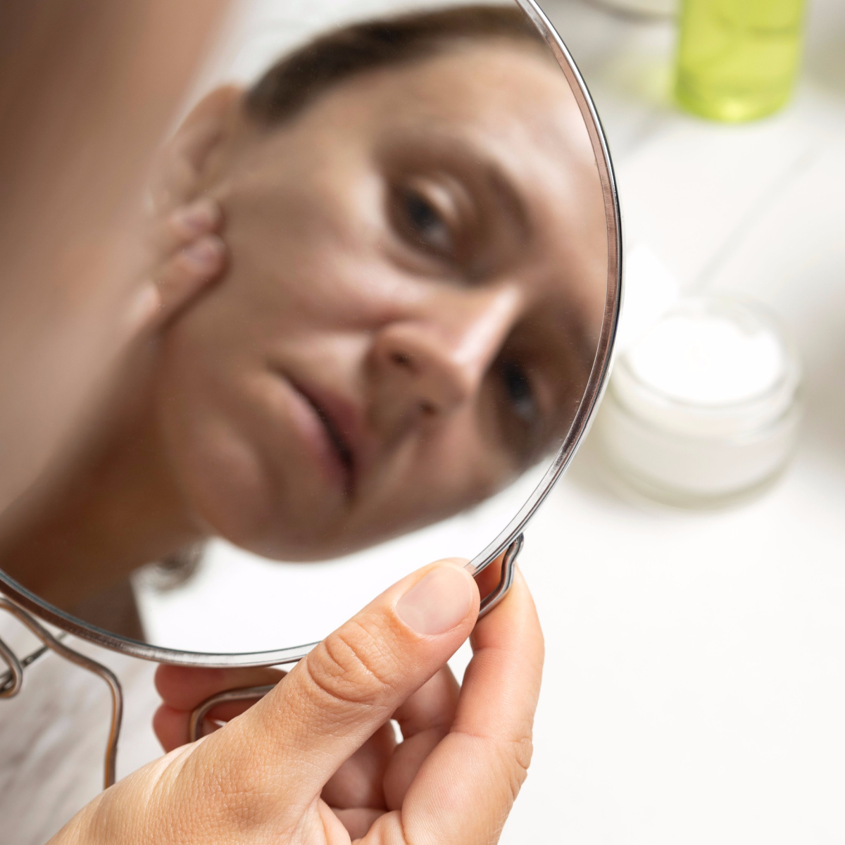 woman looking in mirror with sun spots damage sunscreen white table