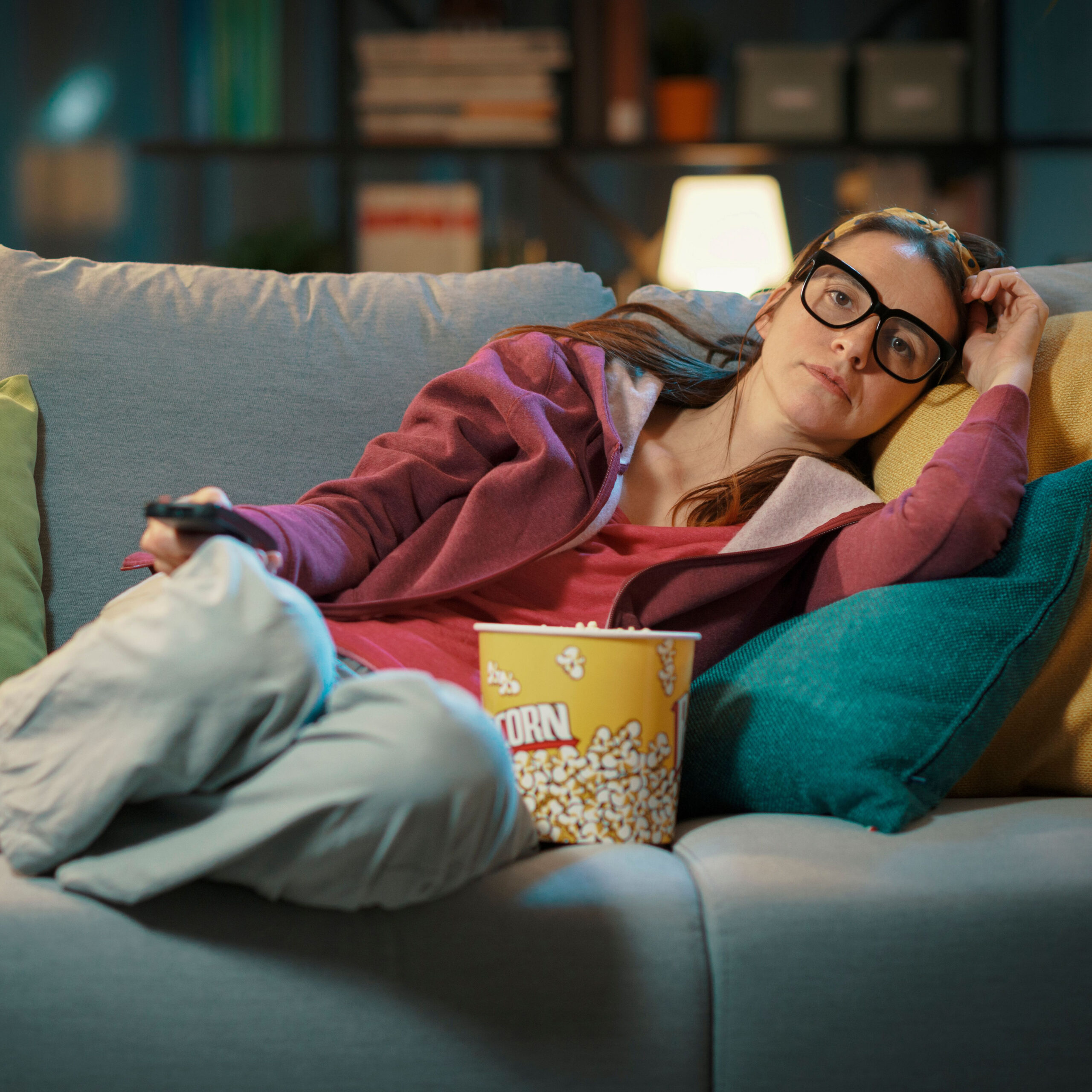 woman being lazy on couch with a bucket of popcorn