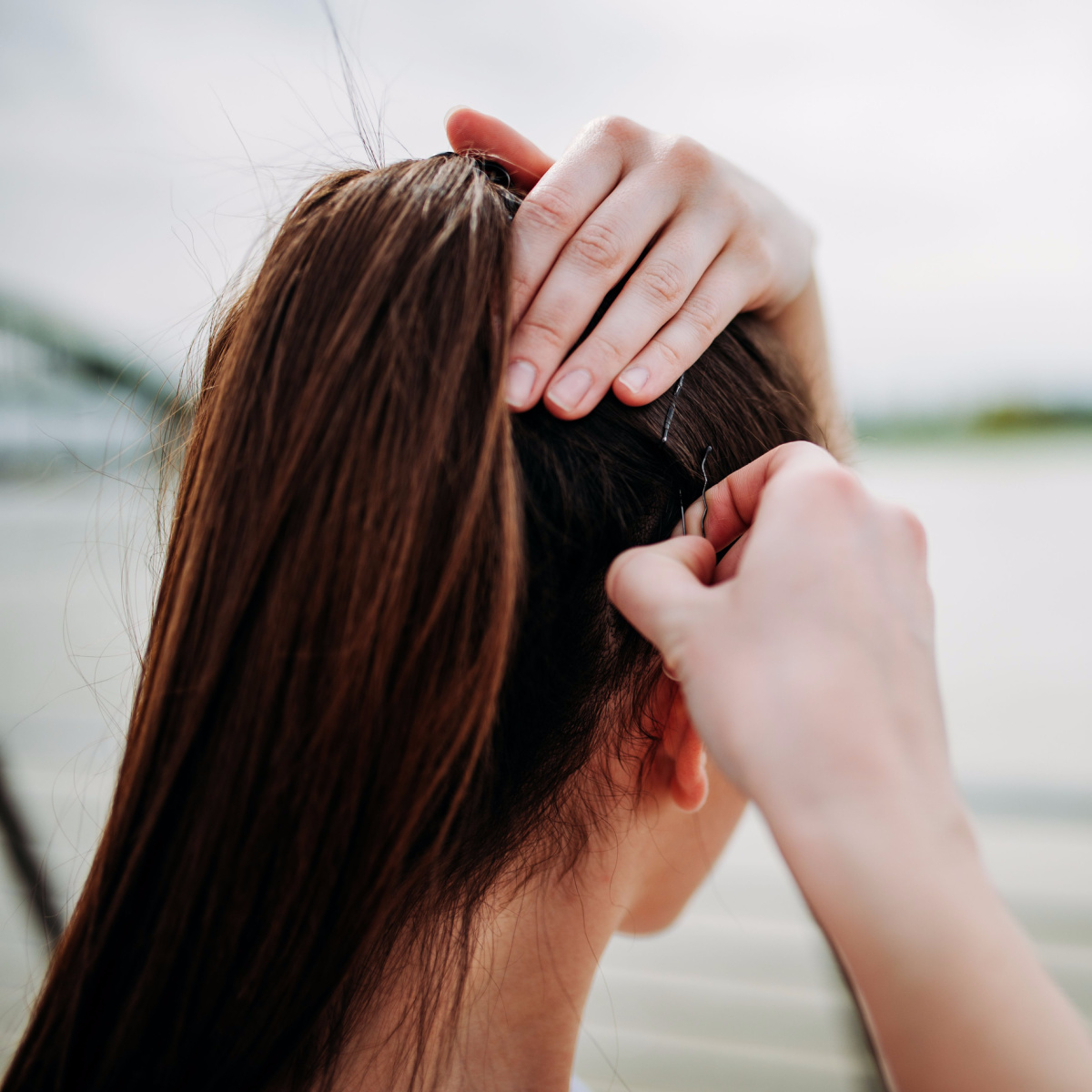 woman pinning bobby pins in long brown hair back up in ponytail from behind