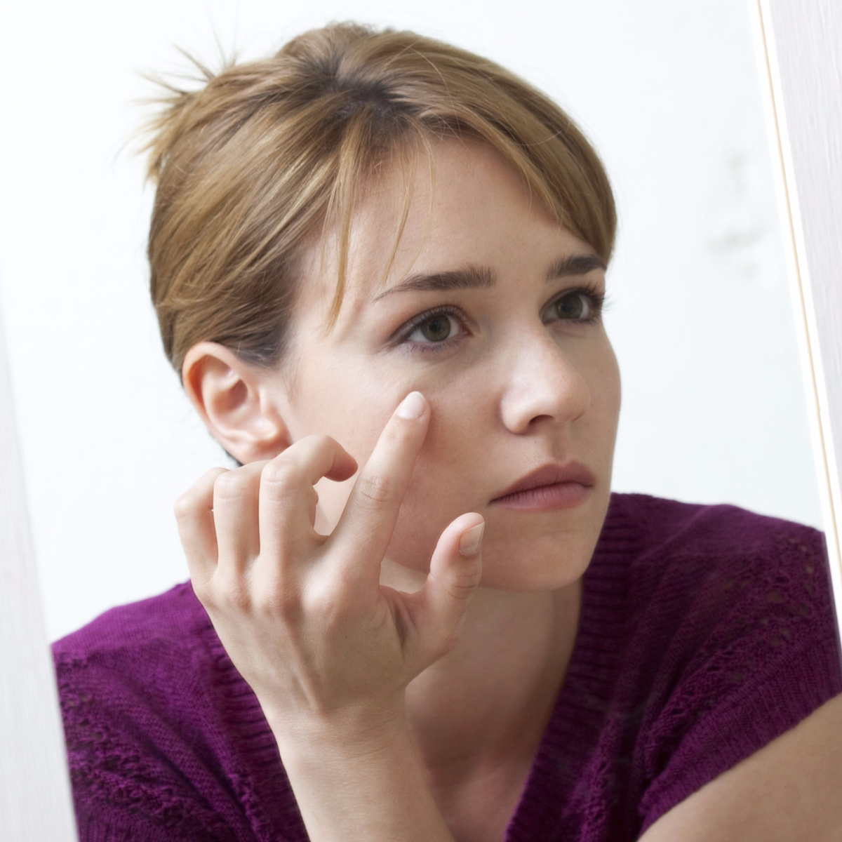 woman looking in mirror touching dark eye circles eye bags skin