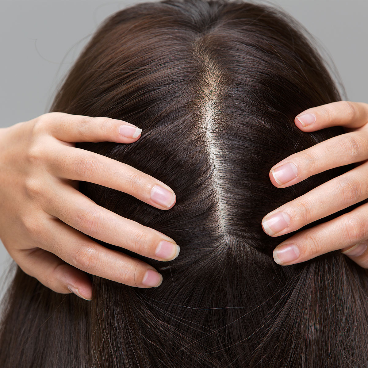 woman parting her shiny brownhair in center middle part scalp health