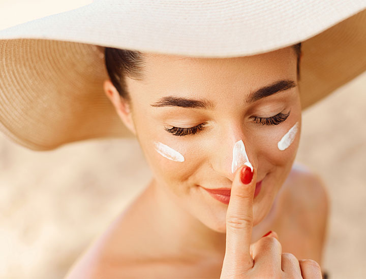 woman-wearing-hat-applies-sunscreen