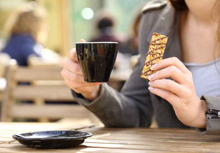 Woman eating granola bar and drinking coffee