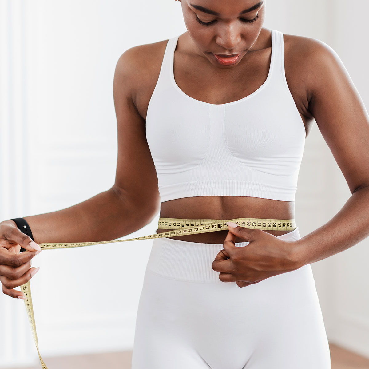woman white sports bra measuring abdomen with measuring tape