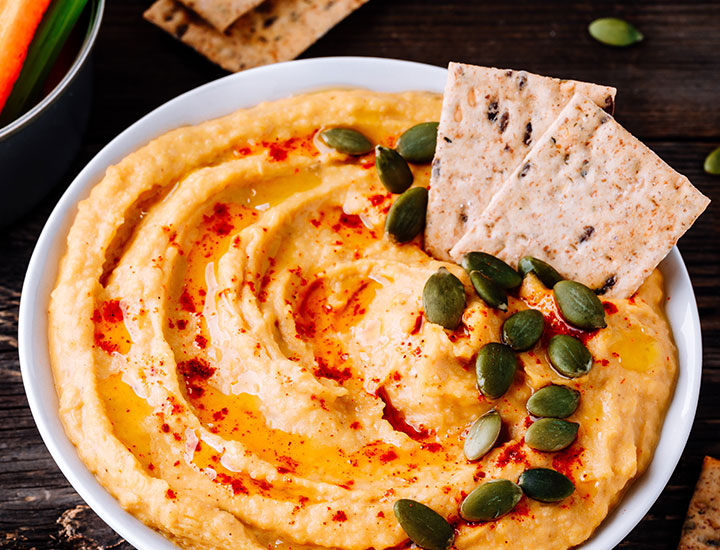 bowl of fresh pepper hummus with pepitas and crackers