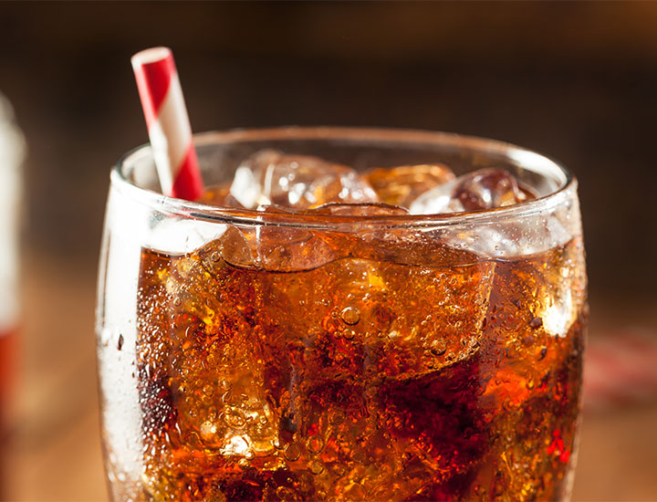 glass of bubbly brown cola soda close-up red-and-white paper straw