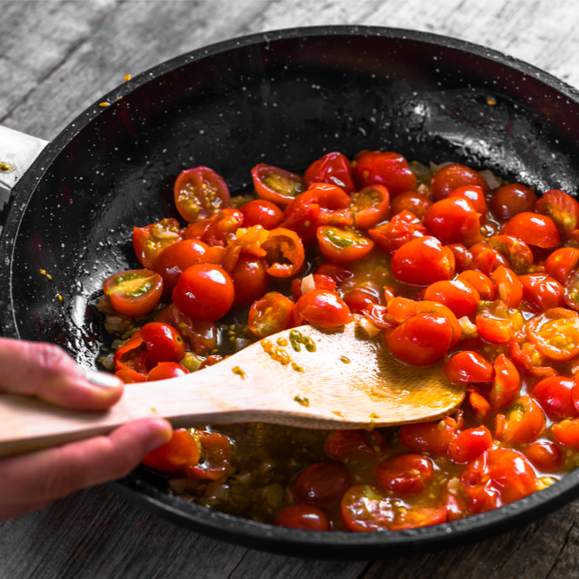 cooking tomatoes in black pan wooden spoon