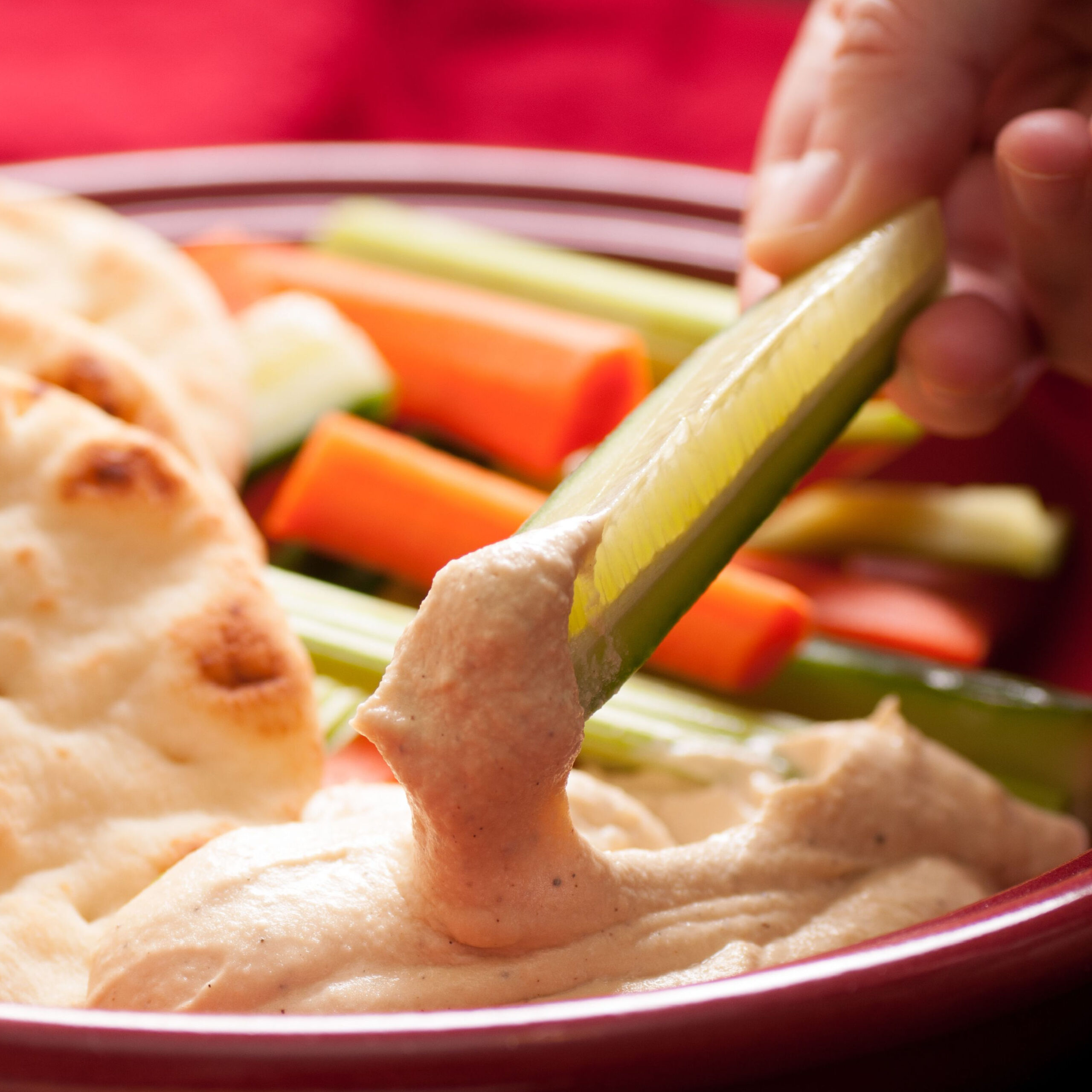 person dipping cucumber into hummus