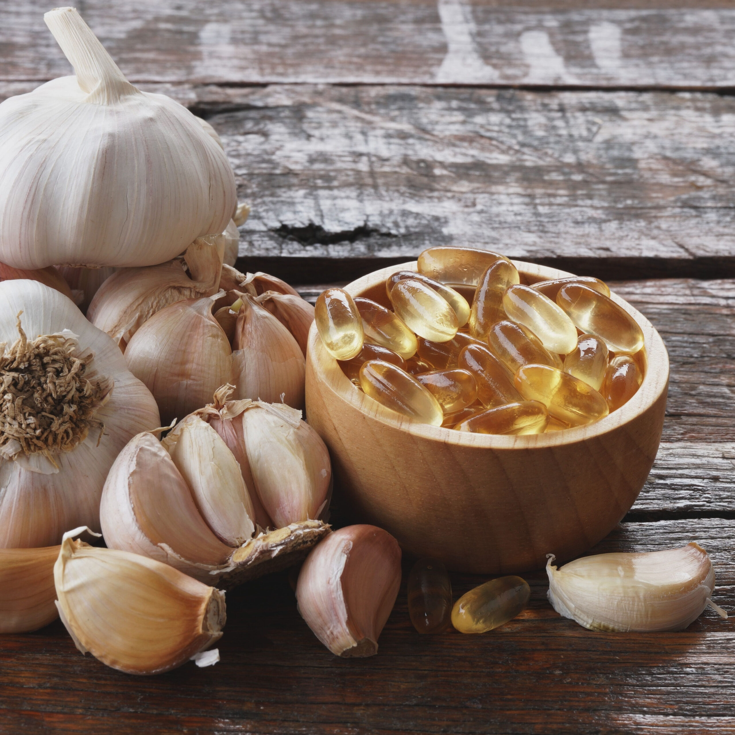 garlic supplements in small bowl beside heads of garlic