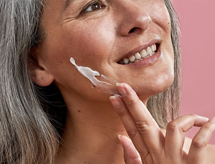 mature woman applying sunscreen wrinkles cheek gray hair