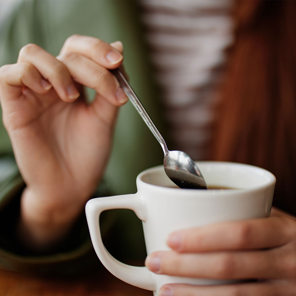 woman stirring coffee with metal spoon white coffee mug