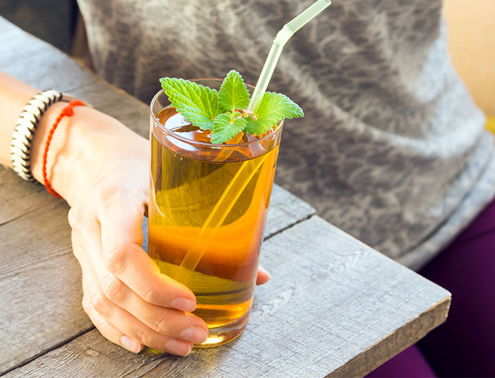 woman holding a kombucha in a glass with a straw
