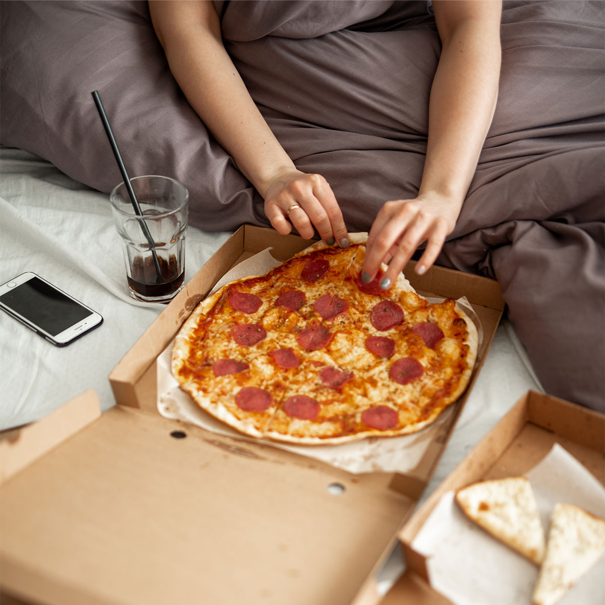 woman eating pizza and soda in bed