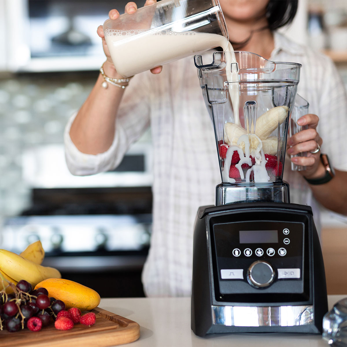 woman adding milk to berry banana smoothie in blender