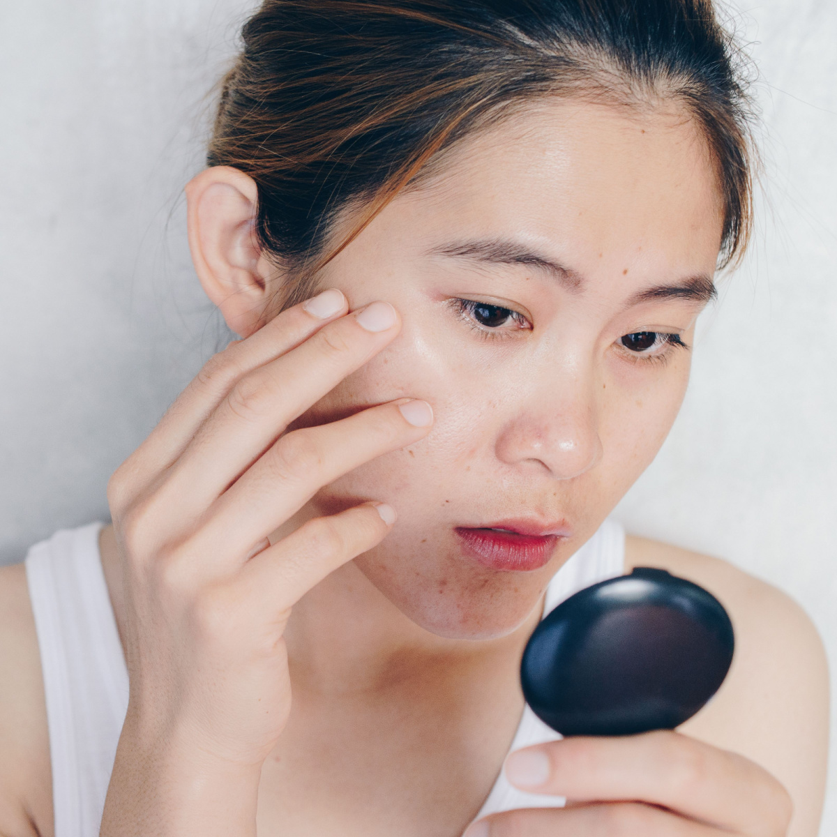 woman touching dark spots face compact mirror