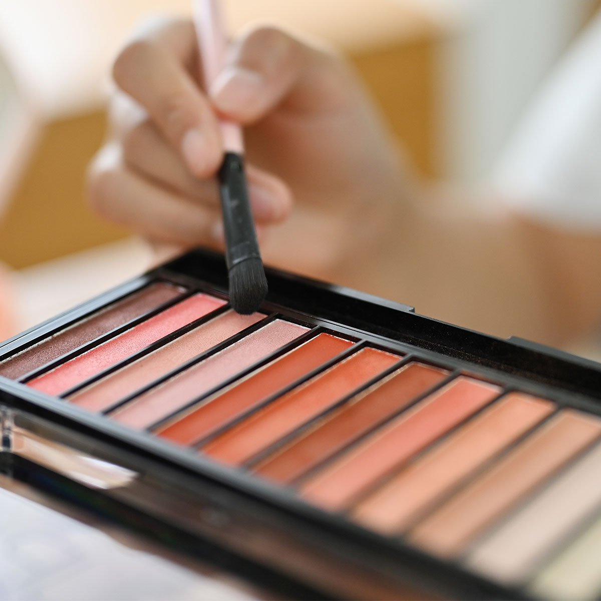 woman dipping brush into shimmery neutral eyeshadow palette