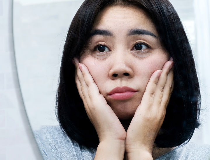 woman looking upset about puffy eyes in the mirror reflection