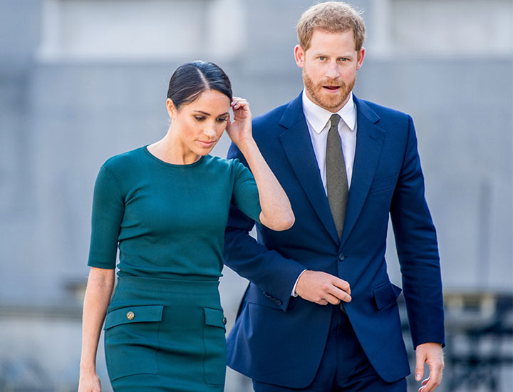 Prince Harry and Meghan Markle looking disappointed wearing blue