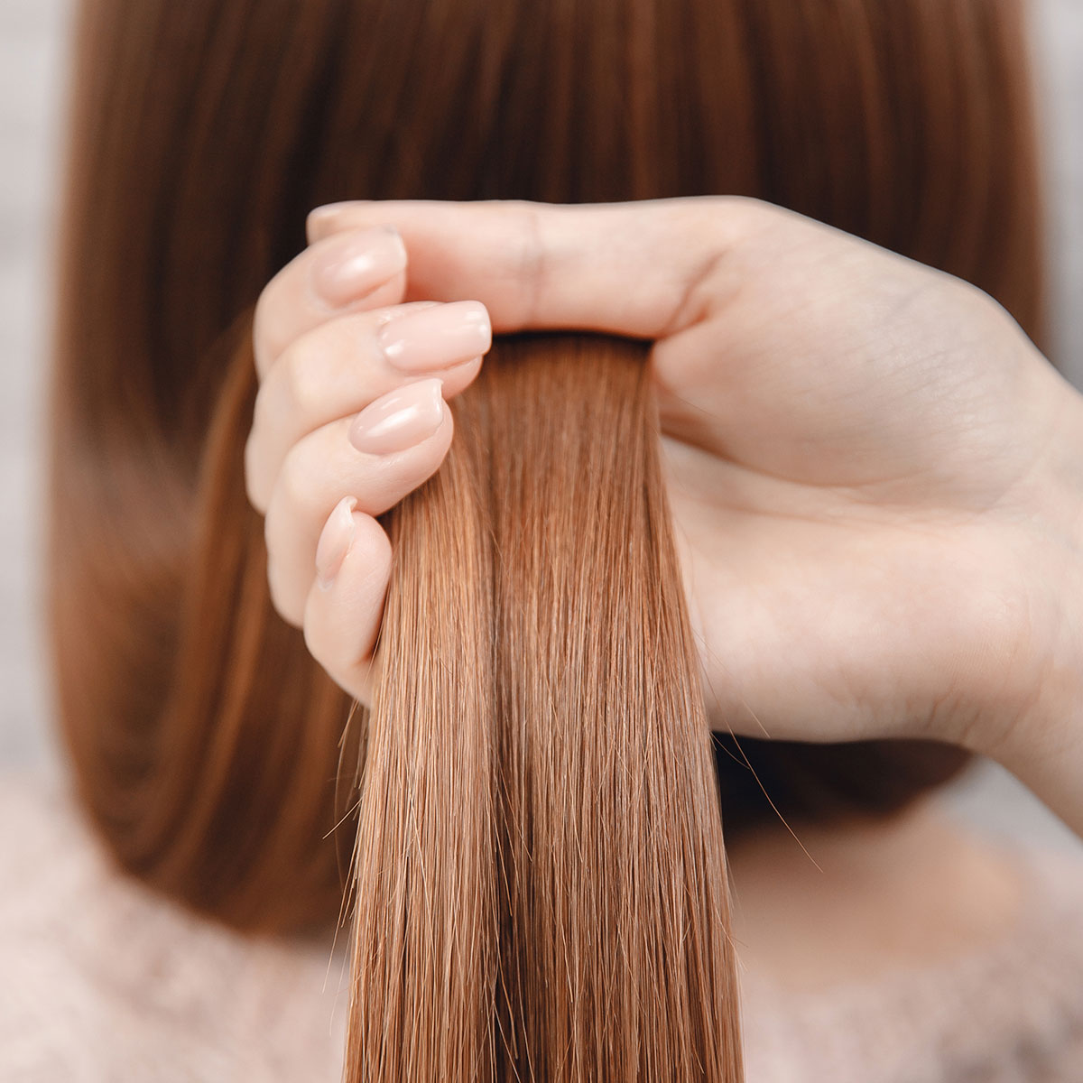 hand holding section of smooth soft red light hair in hands