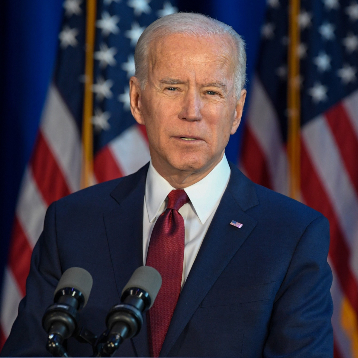 president joe biden speaking podium suit red tie american flag background the white house