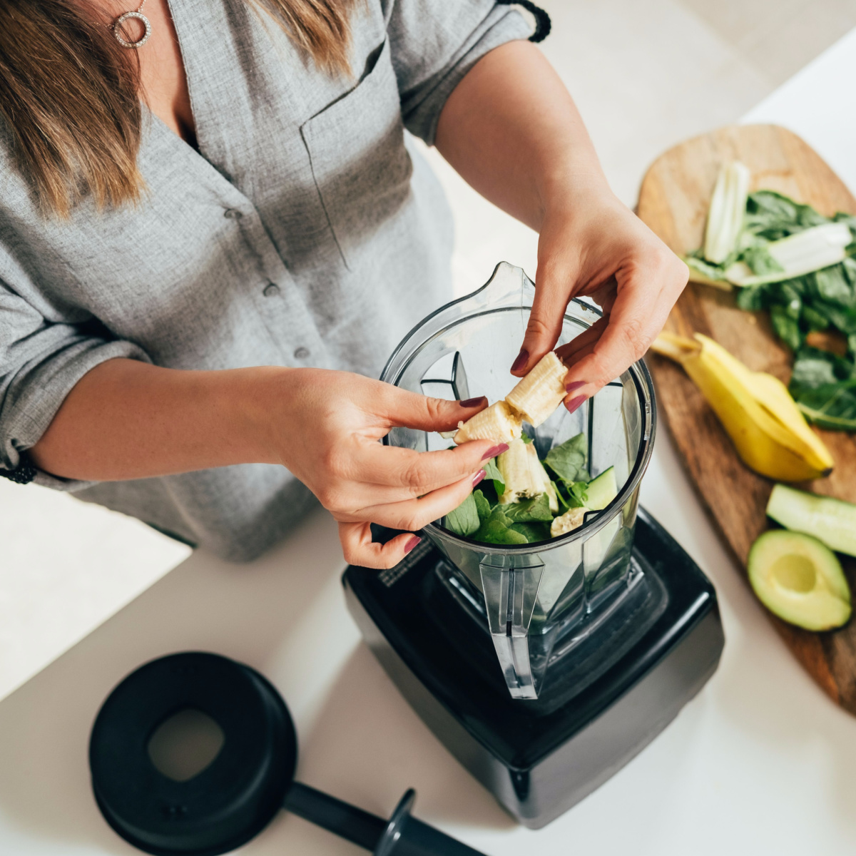 woman making banana smoothie tossing ingredients into blender