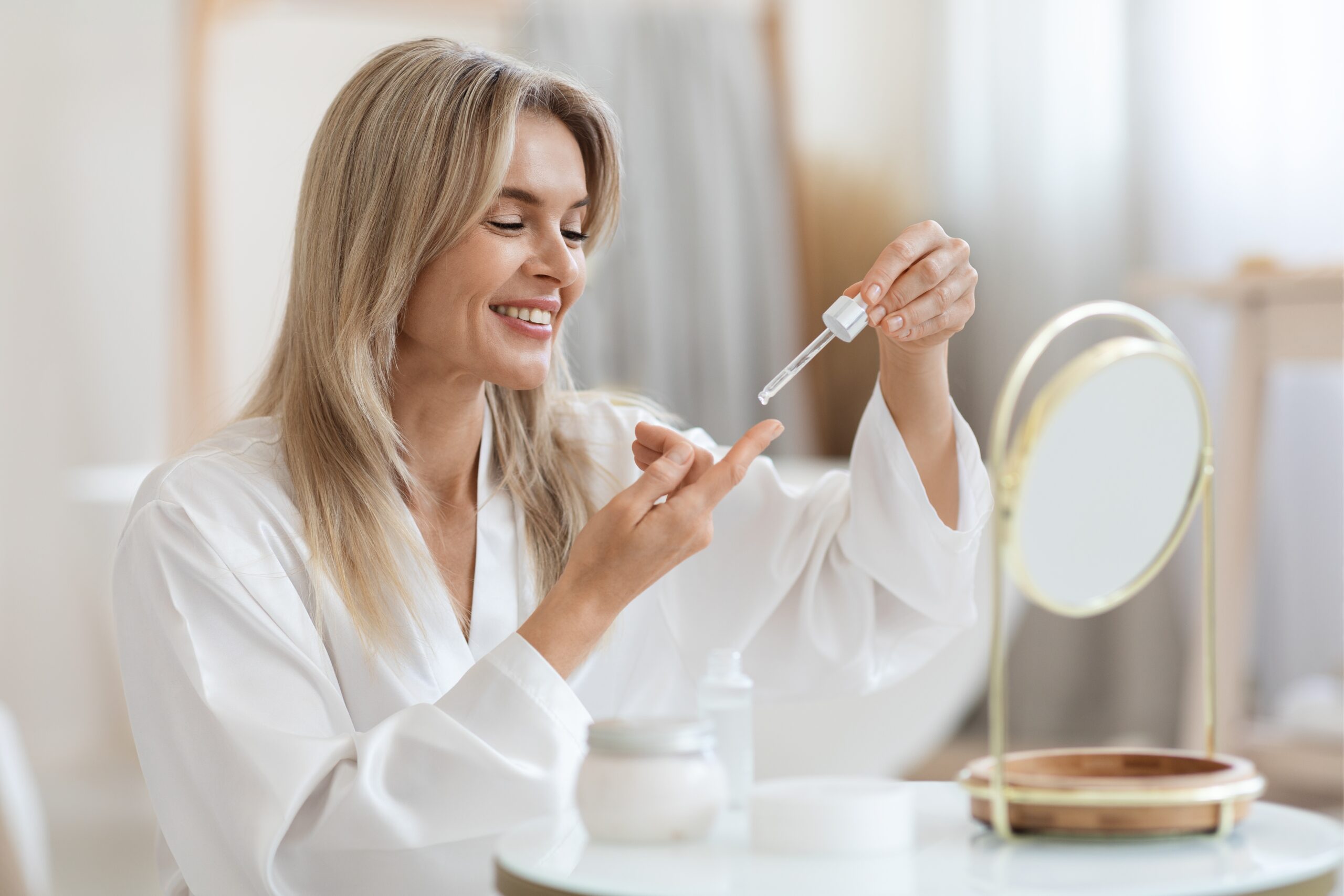 woman adding serum to finger about to apply to face mirror white robe