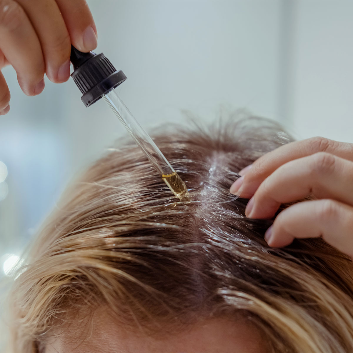 woman applying hair serum to scalp with dropper