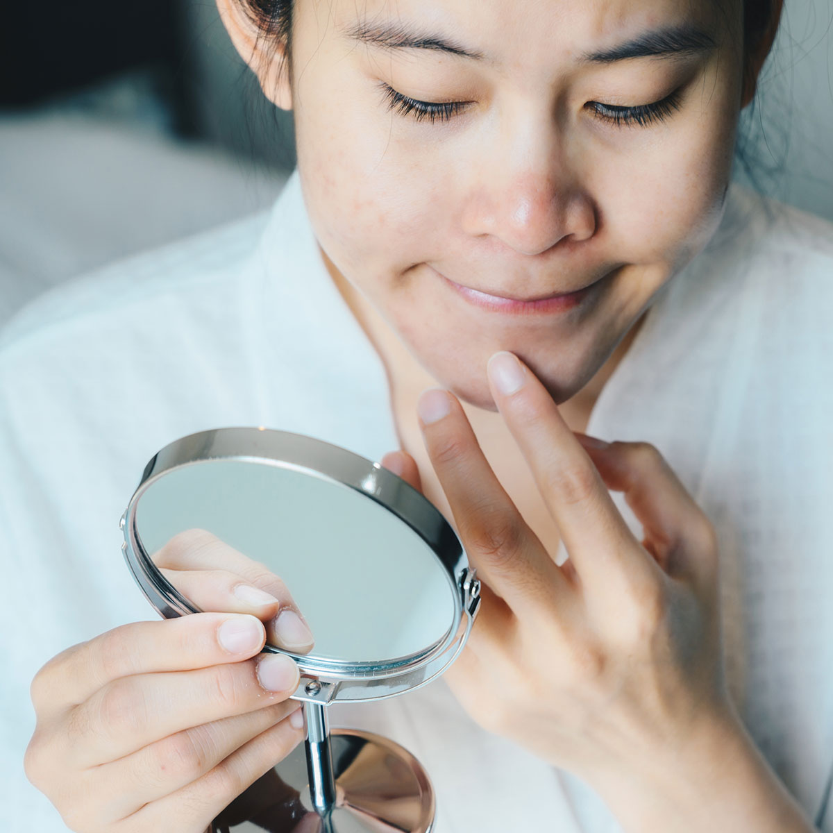 woman checking her skin chin in the mirror touching face white robe
