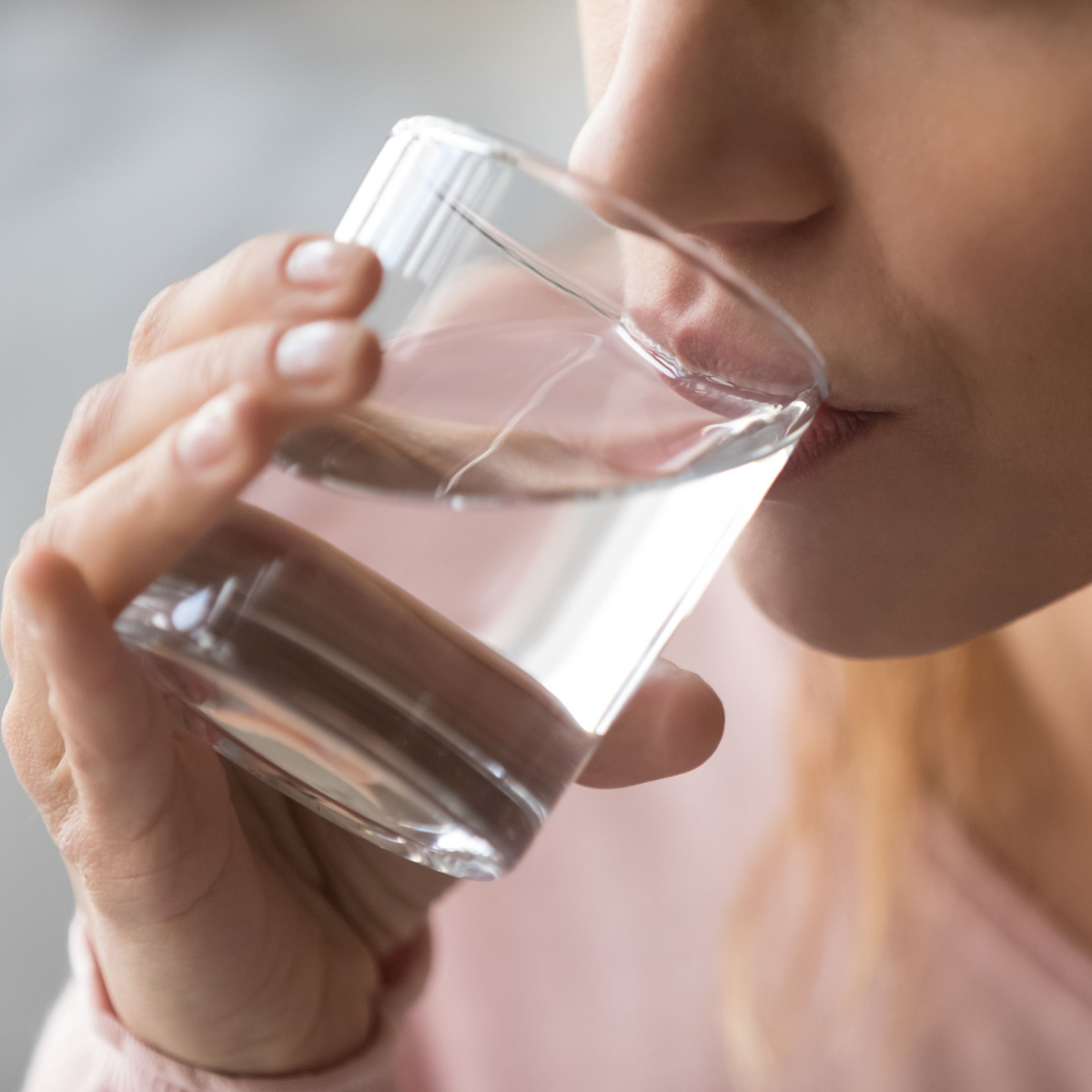 woman drinking water from glass close up pink shirt