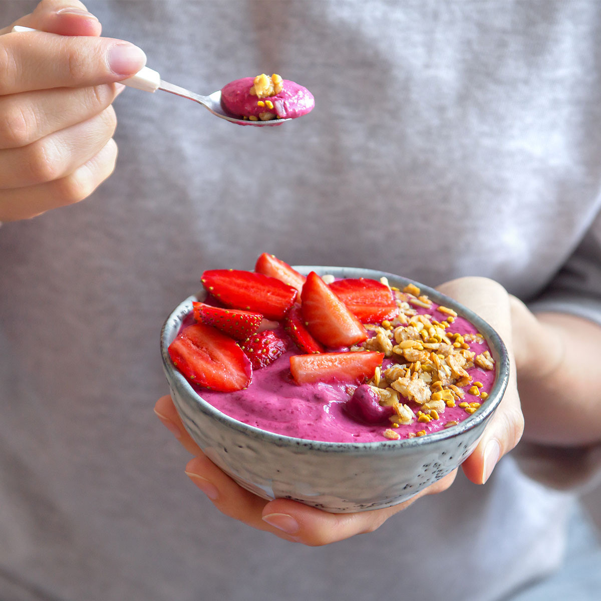 woman eating acai bowl topped with berries nuts and seeds