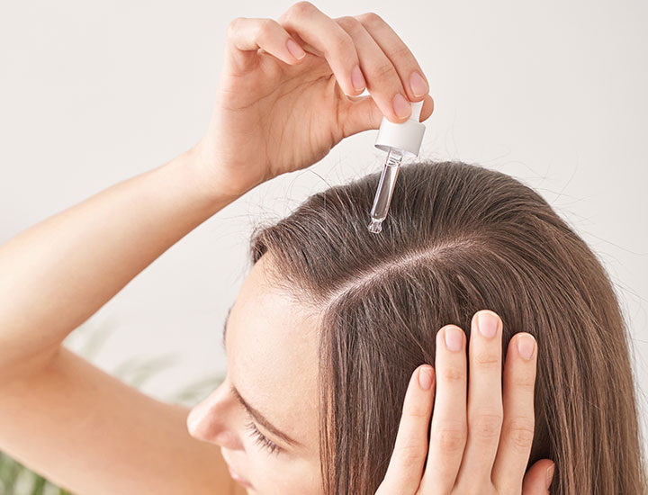 woman applying scalp oil to head holding down hair dropper