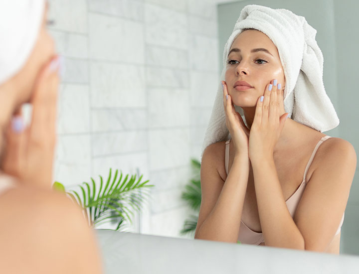 woman touching face applying sunscreen mirror towel