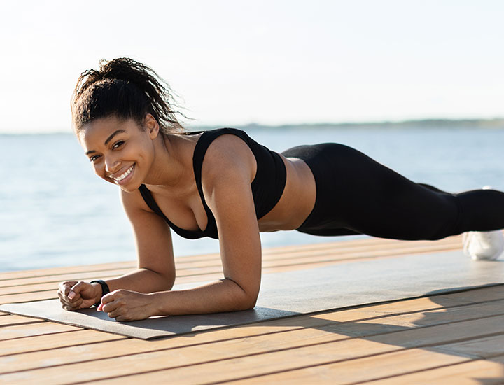 young woman doing planks by ocean