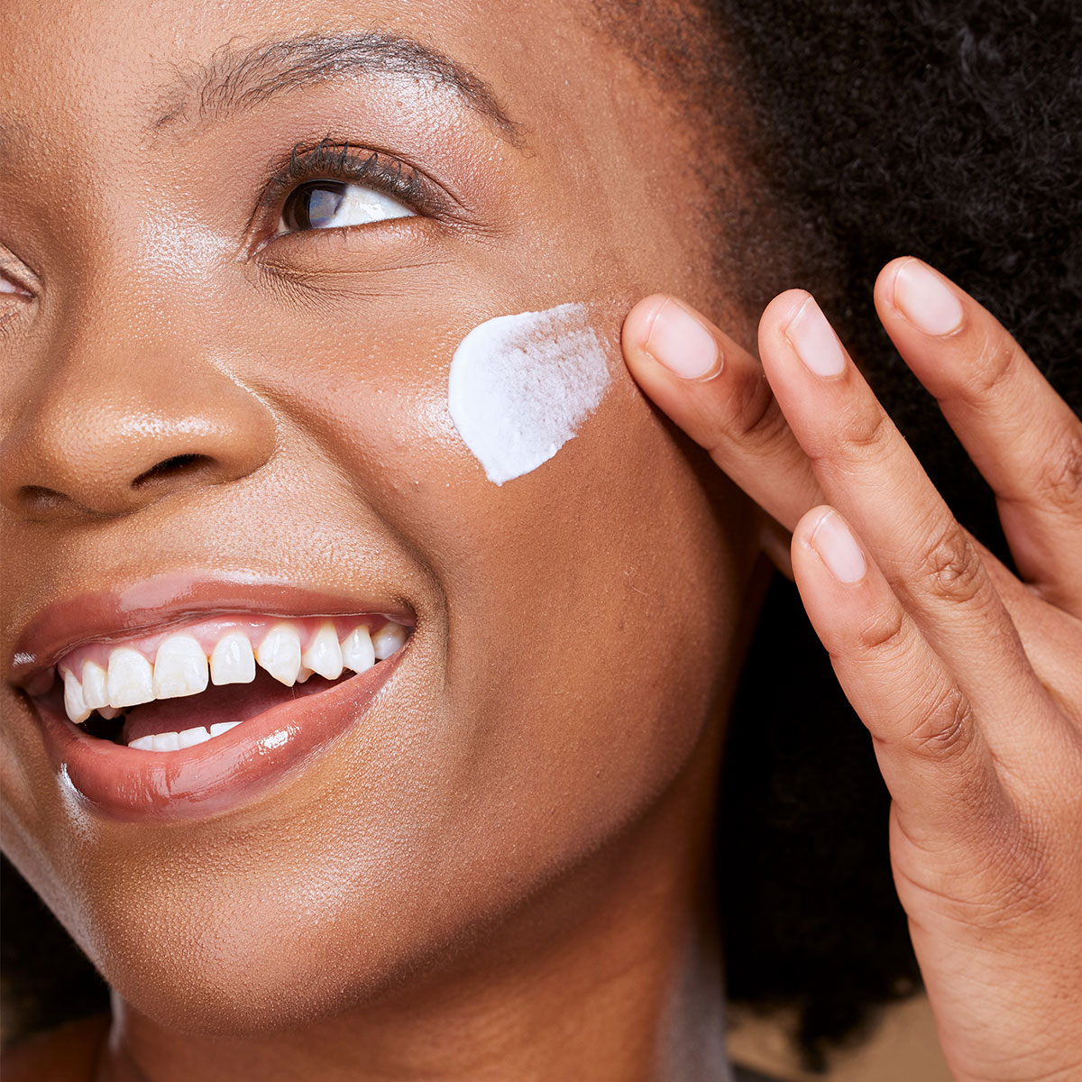 closeup shot of a woman applying white dollup of sunscreen to cheek with finger