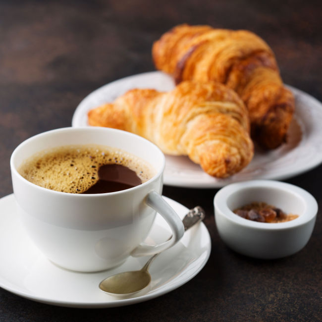 cup of coffee beside plate of croissants