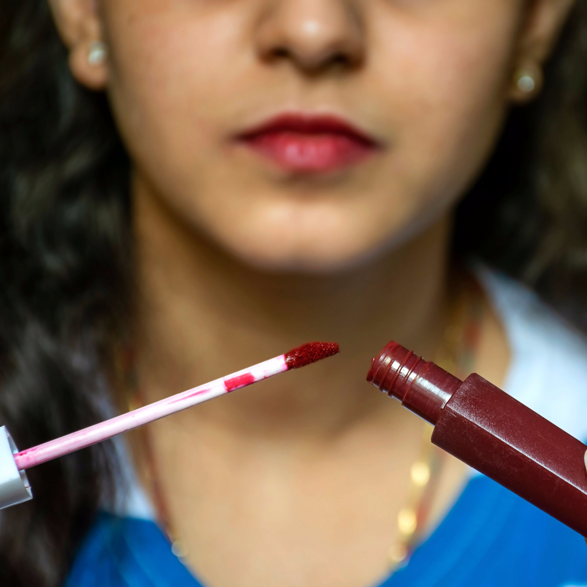 woman opening dark red matte lipstick tube about to apply with wand