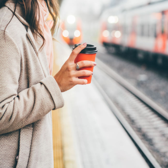 woman standing at train station holding to-go cup of coffee