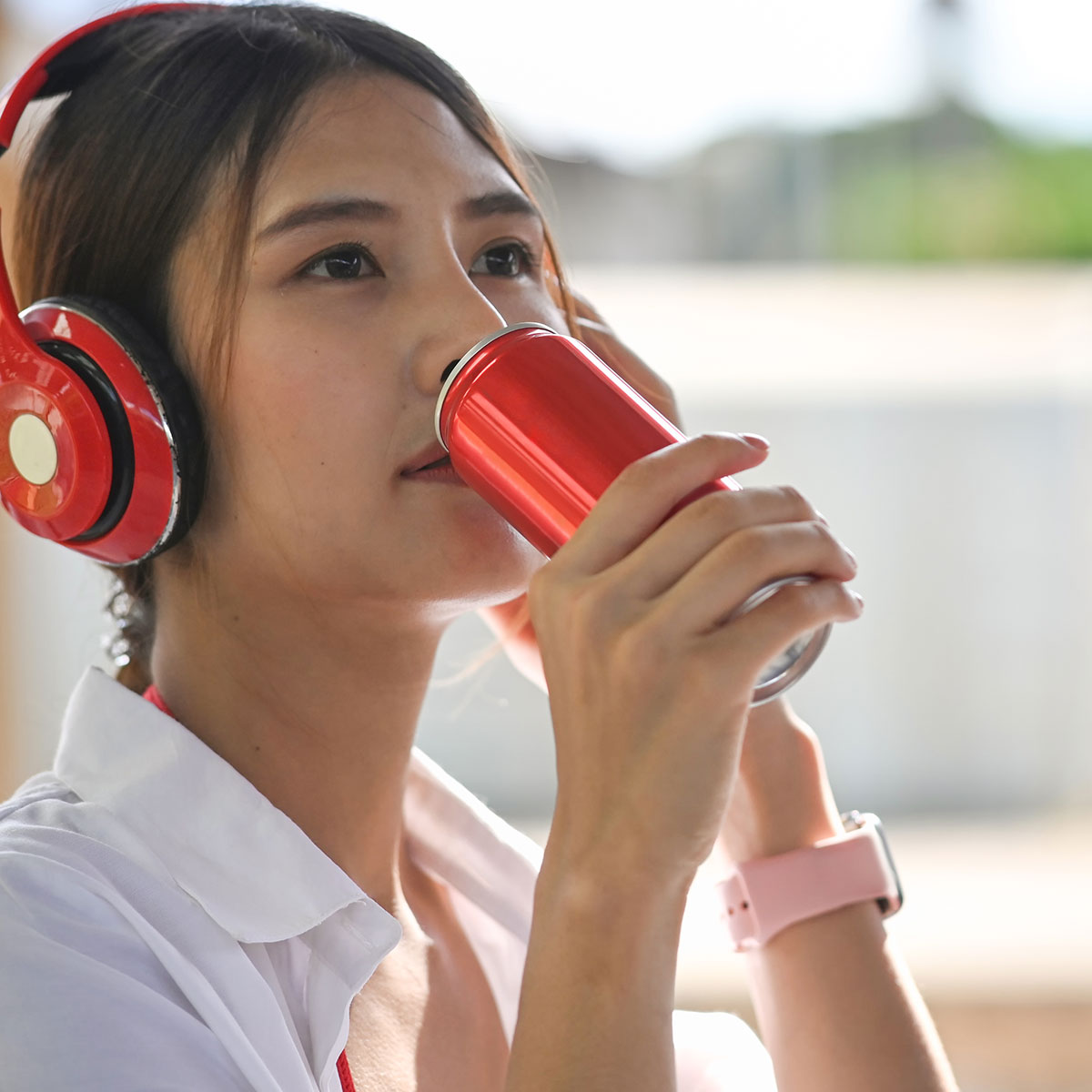 woman sipping on red energy drink wearing headphones outside