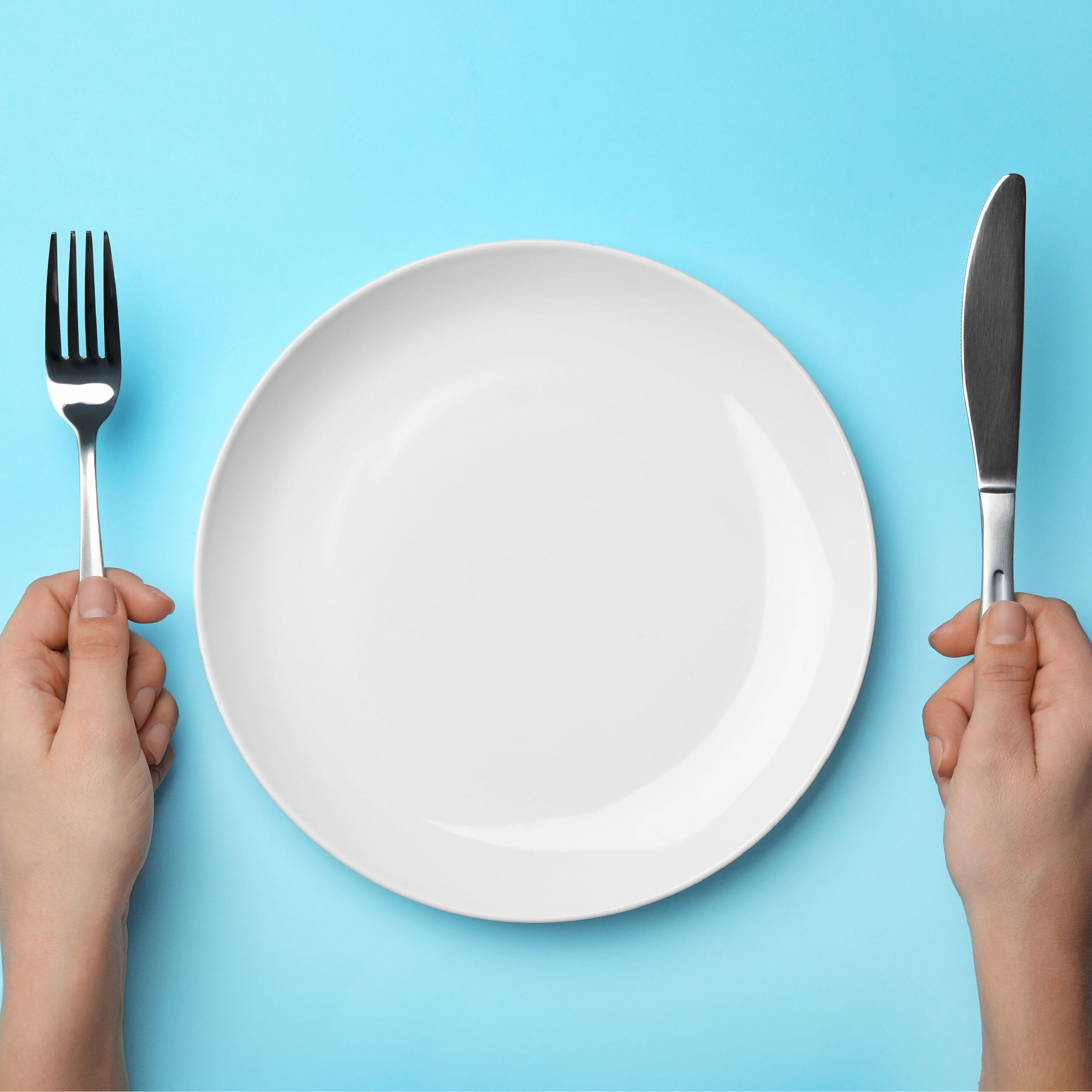 person holding utensils at empty plate