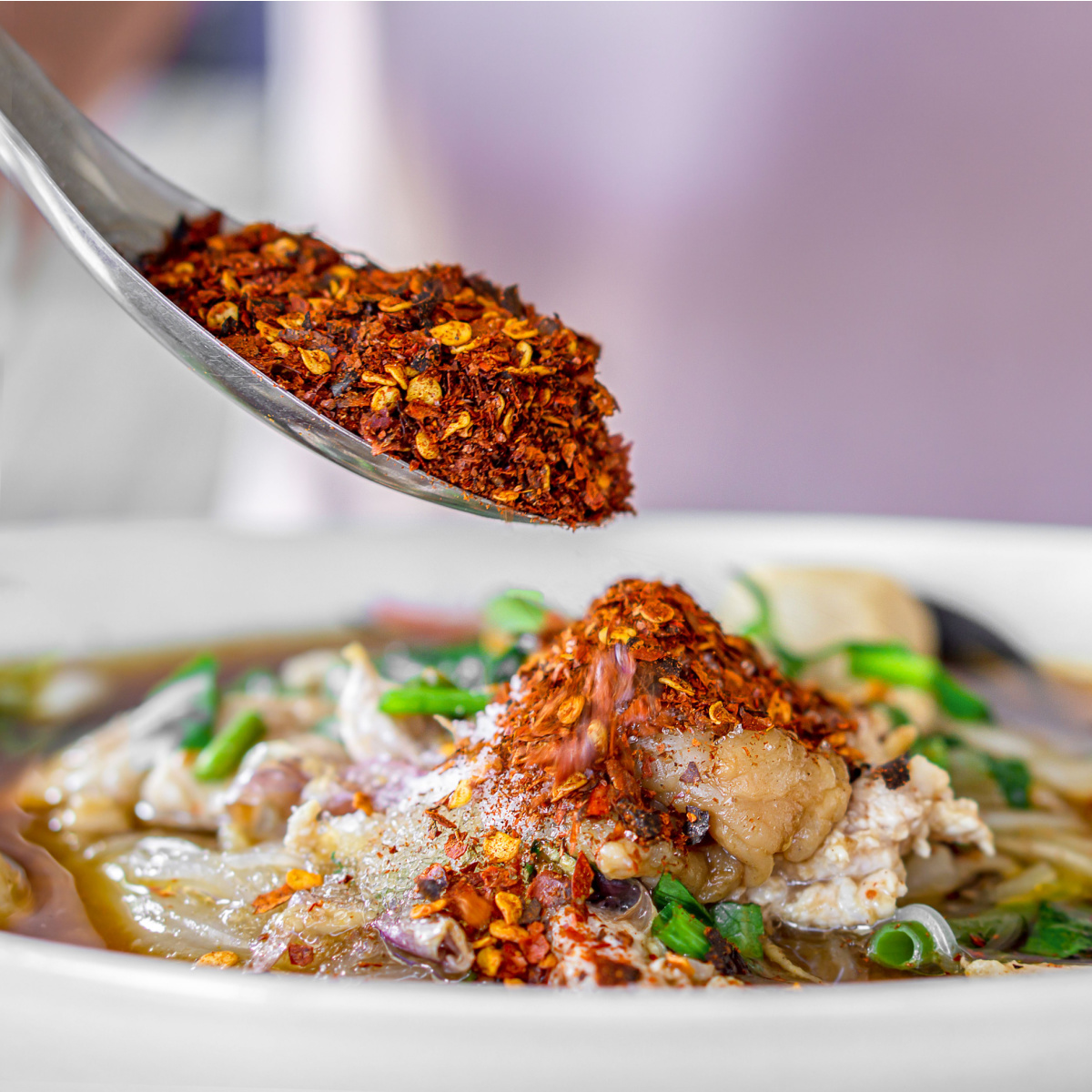 person pouring red chili powder in soup